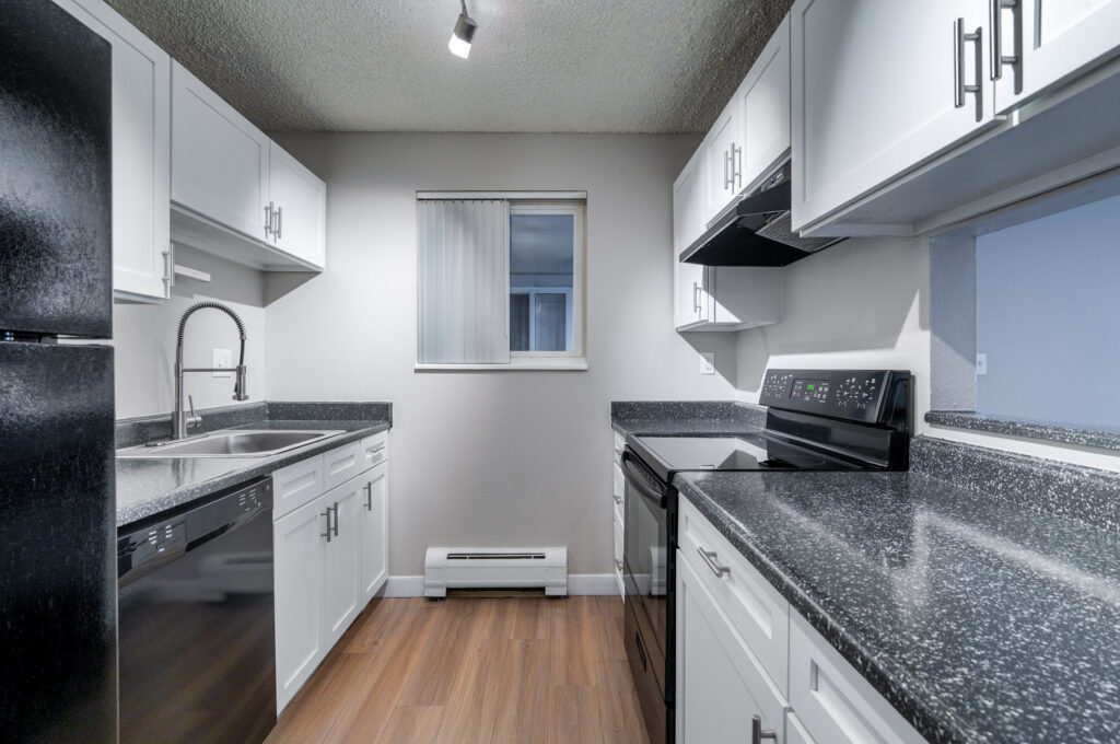 Modern kitchen with black appliances, white cabinets, granite countertops, wood flooring, and a window with vertical blinds. The space is clean, well-lit, and organized with ample storage and workspace.